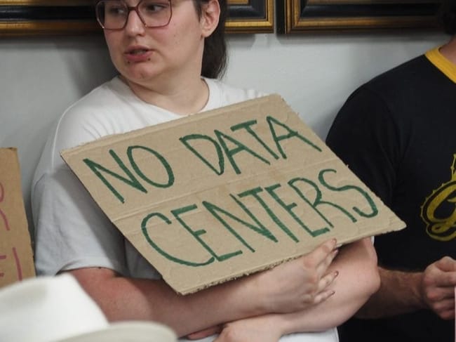 An audience member attending a Pulaski County, Arkansas, Quorum Court agenda-setting meeting holds a sign opposing data centers on June 9, 2026. (Photo by Ainsley Platt/Arkansas Advocate)