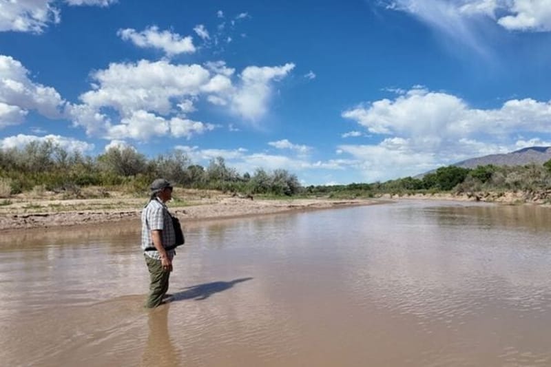 A man stands in the Rio Grande north of Albuquerque, N.M., after summer storms briefly bumped up flows in mid-June. New research suggests climate change could nearly double the costs of household water in some American cities. (Photo by Laura Paskus/Source New Mexico)