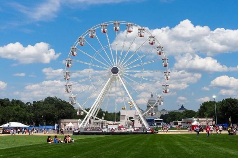 Attendees sit in the grass in front of the Ferris wheel at the Trump administration's Freedom 250 Great American State Fair on the National Mall on Thursday, June 25, 2026. (Photo by Ashley Murray/States Newsroom)