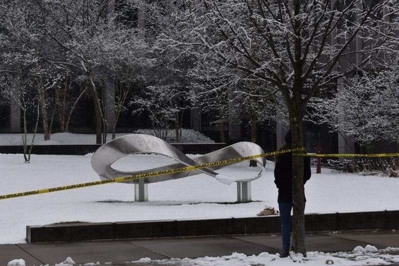 A grad student stands by the sculpture 'Infinite Possibility' outside the Brown University's Engineering Research Center, restricted by crime scene tape, on Dec. 14, 2025, after a mass shooting there. People who carry out mass public shootings often display observable warning signs long before an attack, according to a new study. (Photo by Christopher Shea/Rhode Island Current)
