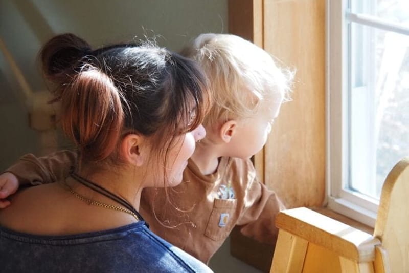 A child care provider and toddler look out the window at Rise for Baby and Family in Keene, N.H. A new analysis of federal data found the gender pay gap between women and men widened last year. (Photo by Maya Mitchell/New Hampshire Bulletin)