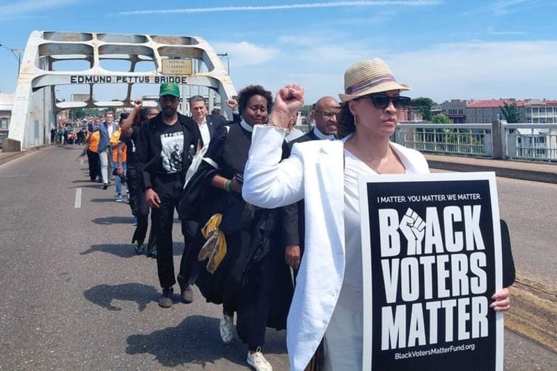 Corey Minor Smith of Canton, Ohio holds a “Black Voters Matter” sign while marching over the Edmund Pettus Bridge in Selma, Alabama on May 16, 2026. Faith leaders gathered in Selma Saturday for a prayer event as part of the “All Roads Lead To The South” protests, aimed at mobilizing voters amid Republican efforts to eliminate majority-minority districts. (Ralph Chapoco/Alabama Reflector)